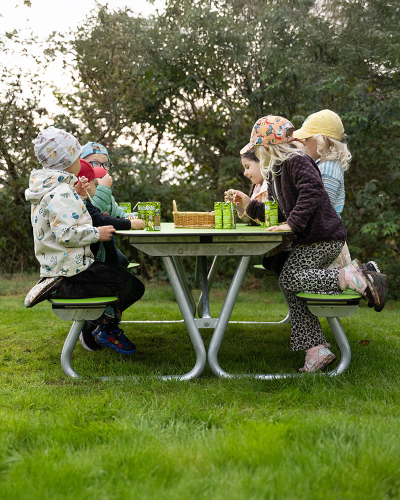 A group of kids on a Hallon picnic table located on a playground.